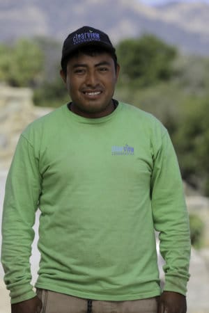 A man in a green shirt standing in front of a mountain.