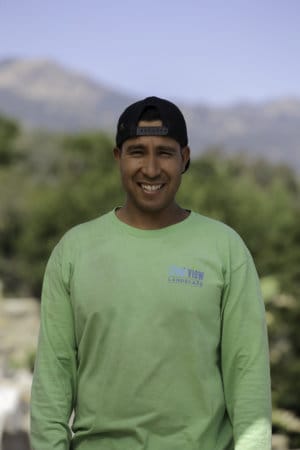 A man in a green shirt smiling in front of a mountain.