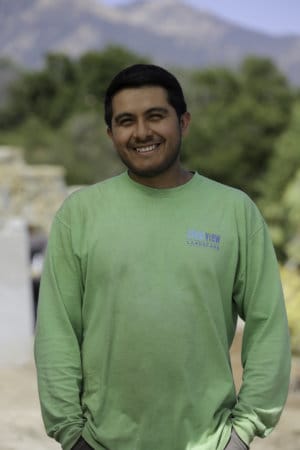 A man in a green shirt smiling in front of a mountain.