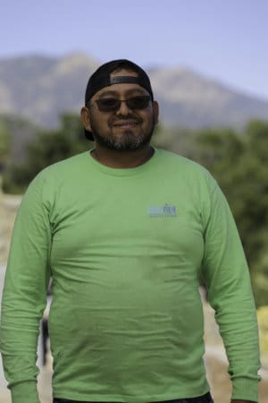 A man in a green long - sleeve shirt standing in front of a mountain.