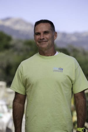 A man in a green t - shirt standing in front of a mountain.