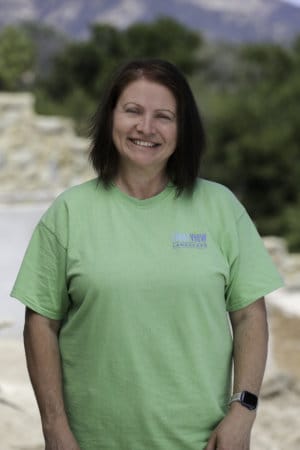 A woman in a green t - shirt standing in front of a mountain.