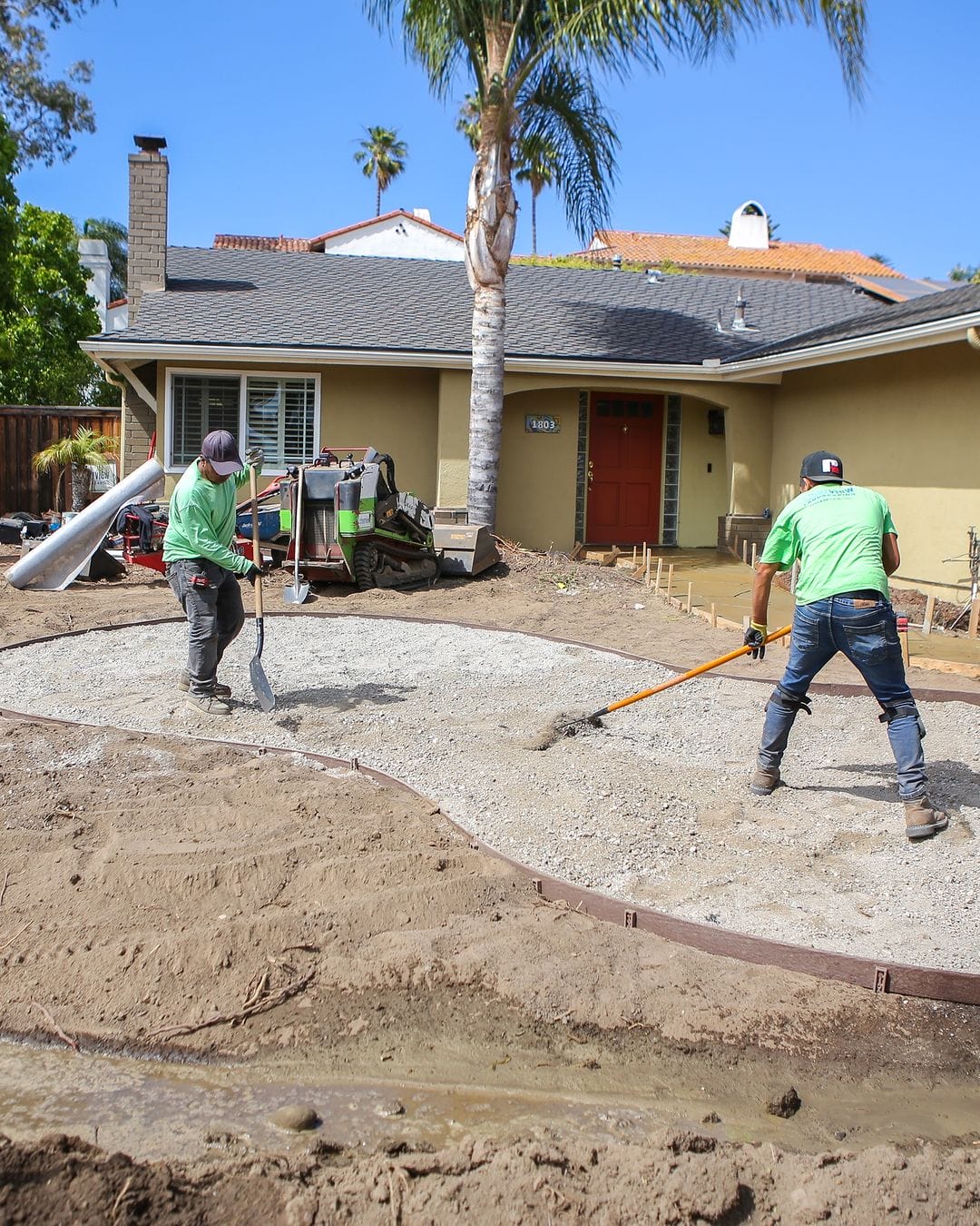 Two men working on a concrete patio in front of a house.
